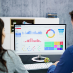 Two people sitting in front of a computer with KPIs