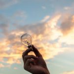 Hand hält Glühbirne bei Abendröte